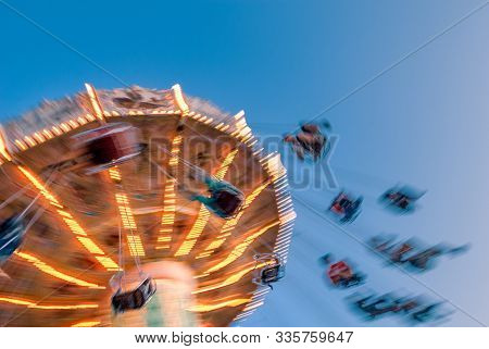 Amusement Park Motion Blurred Riders On Retro Vintage Tilting Swing Against Clear Blue Sky.