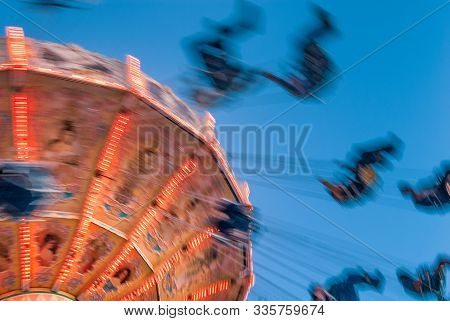 Amusement Park Motion Blurred Riders On Retro Vintage Tilting Swing Against Clear Blue Sky.