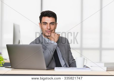 Smiling Handsome Caucasian Businessman In Black Suit Support The Chin In Modern Office.
