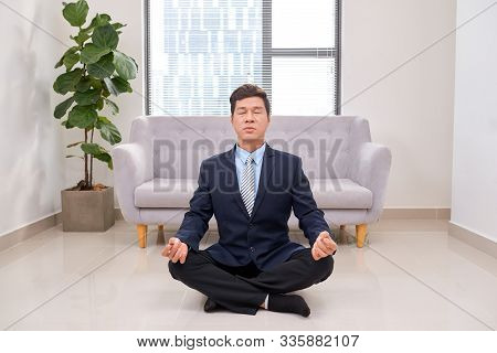 Businessman Meditating In Lotus Pose On The Floor In The Office