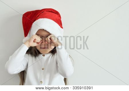 Sad Little Girl In A Christmas Santa Hat. Child Isolated On A White Background. Christmas, New Year 