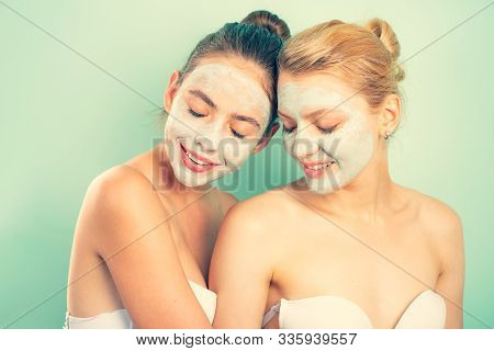 Friendly Young Beautiful Girls With Bare Shoulders Apply Organic Face Mask And Smile. Blond And Dark