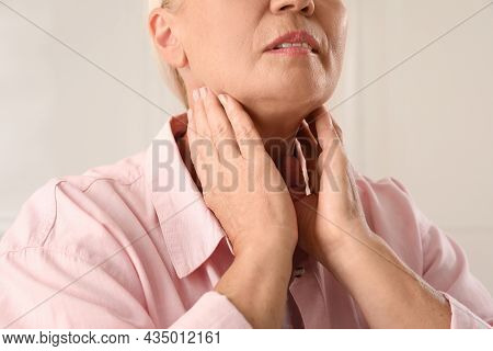 Mature Woman Doing Thyroid Self Examination On Light Background, Closeup