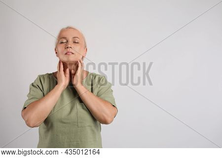 Mature Woman Doing Thyroid Self Examination On Light Grey Background, Space For Text