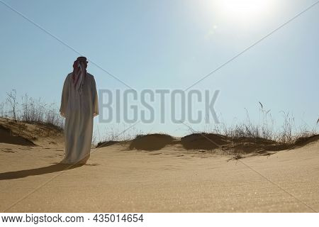 Man In Arabic Clothes Walking Through Desert On Sunny Day, Back View