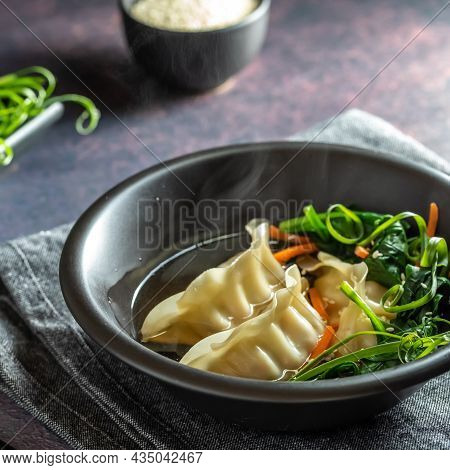 Close Up Of A Bowl Of Dumplings In Steaming Broth With Greens And Sesame Seeds, Ready For Eating.