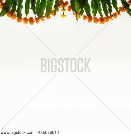 Garland of a marigold flowers and mango leaves hung on white background. Hindu festive elements and template for festival season.