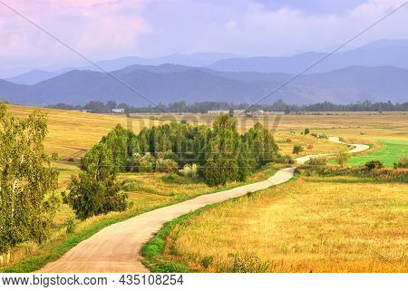 A Winding Gravel Road In A Field Under The Evening Blue Sky. Altai, Siberia, Russia