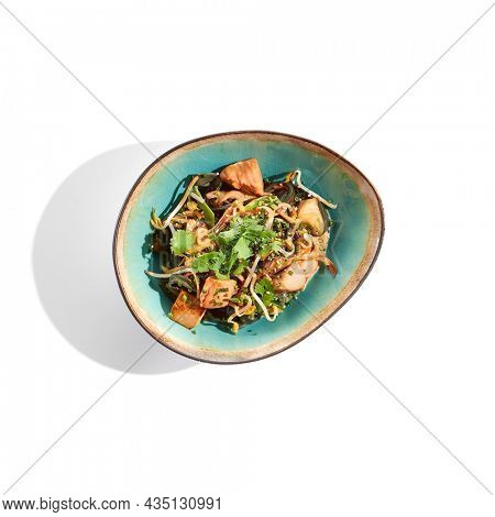 Pan asian food - chicken udon with mushrooms on white background. Noodle with chicken  on wok in asian style. Indonesian wok with black udon noodles and chicken in ceramic bowl