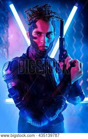 Cyberpunk warrior portrait in neon light background. A brave cyberpunk man poses in a protective uniform standing on alert with a gun. Game, virtual reality.