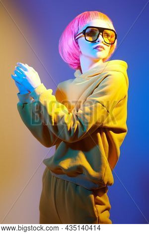 Youth fashion and beauty trends. Confident modern girl with bright pink hair poses in yellow sunglasses and yellow hoodie set in mixed color light. Sport chic fashion. 