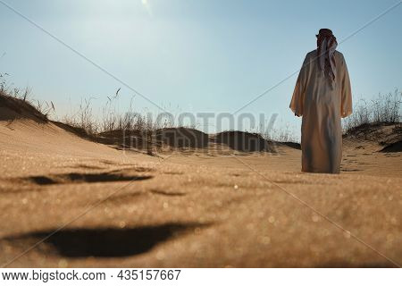 Man In Arabic Clothes Walking Through Desert On Sunny Day, Back View