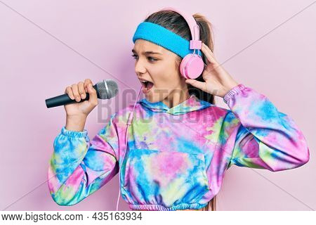 Young brunette girl singing song using microphone wearing sportswear angry and mad screaming frustrated and furious, shouting with anger. rage and aggressive concept. 