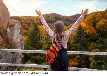 Woman Traveler With Backpack Stands By Rocks In Tustan Raising Arms In Autumn Carpathian Mountains. 