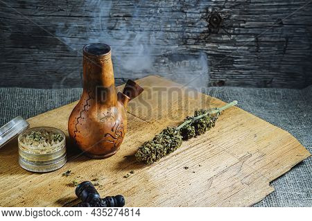 Old Brown Steamung Bong And Open Cannabis Grinder With Chopped Marijuana Weed And Medical Cannabis I
