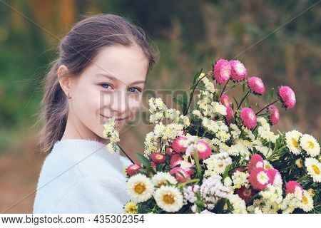 Happy Teenage Girl In A Forest Glade Holding A Huge Bright Bouquet Of Flowers In Her Hands.