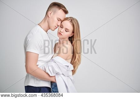 Love concept. Beautiful enamored girl and guy gently hug each other with their eyes closed. Studio portrtait on a white background with copy space.