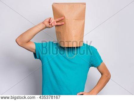 Portrait of teen boy with paper bag over head making Victory gesture. Teenager cover head with bag showing victory sign posing in studio. Child pulling paper bag over head.