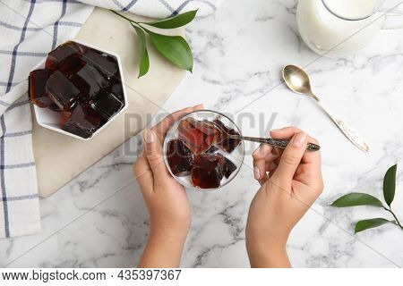 Woman Eating Delicious Grass Jelly Cubes At White Marble Table, Top View