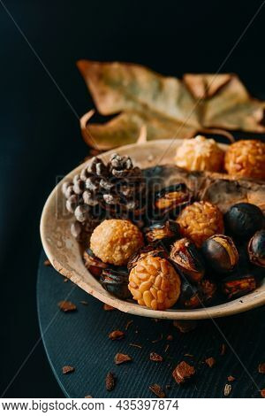 a plate with food traditionally eaten in All Saints Day in Catalonia, Spain, in a party called Castanada, such as roasted chestnuts, roasted sweet potato and panellets, a confection made with marzipan