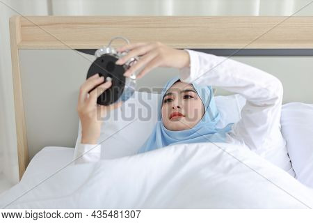 Oversleeping Asian Muslim Woman Wearing White Sleepwear Lying On Bed, Missing Ring Of Alarm Clock Wa