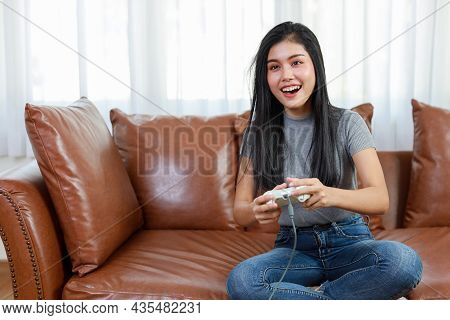 Vdo Game Console Station Concept. Active Asian Woman Sitting On Sofa, Holding Joystick And Playing E