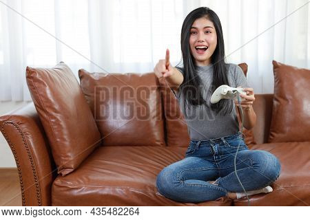 Vdo Game Console Station Concept. Active Asian Woman Sit On Sofa, Holding Joystick And Playing Game 