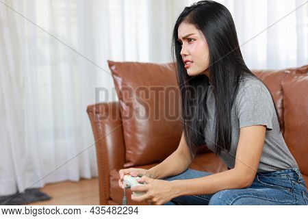 Vdo Game Console Station Concept. Active Asian Woman Sitting On Sofa, Holding Joystick And Playing E