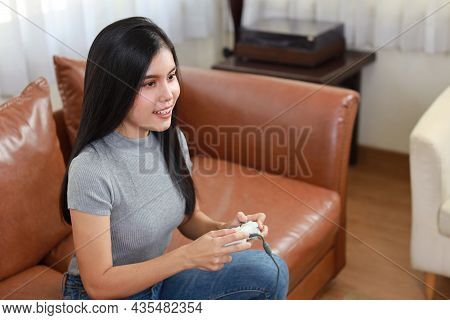 Vdo Game Console Station Concept. Active Asian Woman Sitting On Sofa, Holding Joystick And Playing E