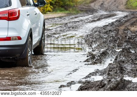 Clean White Suv Car Moving On Dirt Road With Wet Clay In Front Of Blurry Slope At Autumnal Cloudy Da