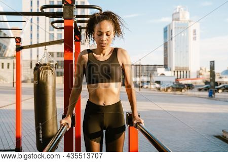 Concentarted young fit african fitness woman exercising on parallel bars at the sportsground