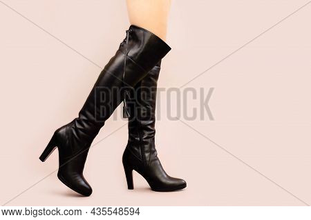 Female Legs In High Black Boots Jackboots On Beige Background. Copy Space, Front View.