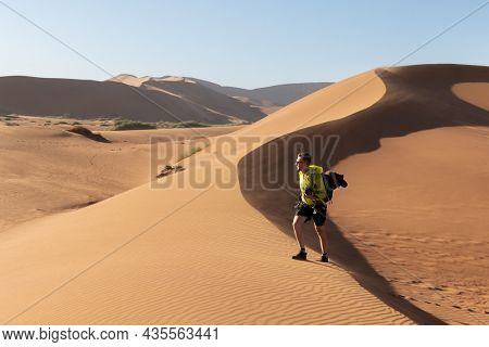 Photographer taking photo in Deadvlei, Namib-Naukluft National Park, Namibia, Africa. Dried ground with sand in Namib desert during sunset. Landscape photography