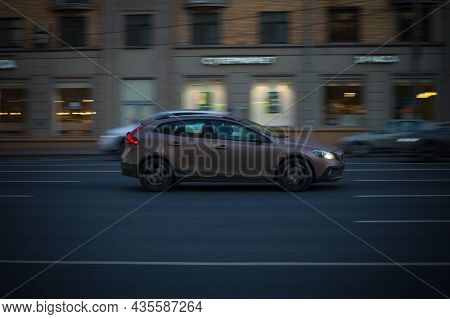 Side View Rolling Shot With Brown  Volvo V40 In Motion On City Street At Night. Evening Driving Alon