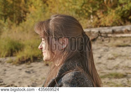 Side View Of Young Woman Smiling And Looking Aside While Sitting In A Forest. Sunny Weekend. Calm An