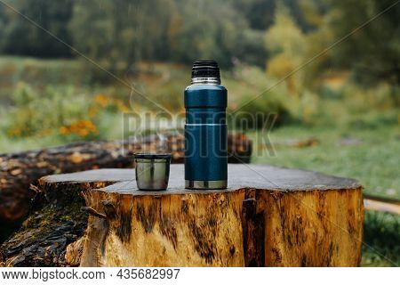 Thermos And Aluminum Hot Drink Mug With Rising Steam Outdoors. Camping Vacuum Flask And Iron Cup Sta