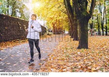 Sincerely Smiling Athletic Woman Have A Jogging In The Autumnal City Park. Young Fitness Female Smil