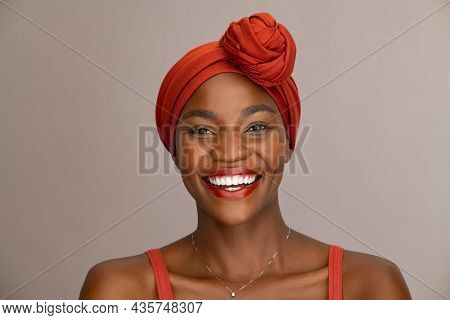 Portrait of beautiful african woman with red headscarf against brown background with copy space. Cheerful black mid woman wearing ethnicity headband. Mature happy lady with traditional clothes.