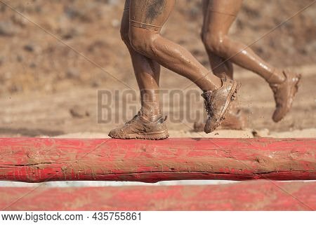 Mud Race Runners. Participants Walking On The Tree Trunk, Catches Balance Above The Pit Full Of Wate
