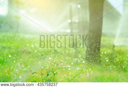 Bokeh Water Splashing On Blur Background Of Automatic Lawn Sprinkler Watering Green Grass. Sprinkler