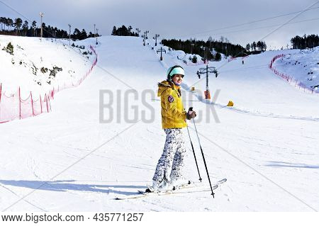 Happy Smiling Young Woman In Yellow Jacket And Ski Helmet Downhill Skiing On A Mountain Slope, Winte