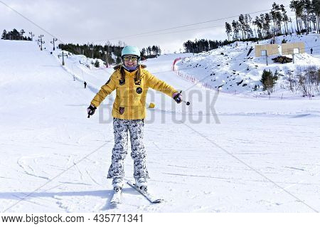 Happy Smiling Young Woman In Yellow Jacket And Ski Helmet Downhill Skiing On A Mountain Slope, Winte