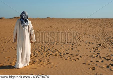 Man In Arabic Clothes Walking Through Desert On Sunny Day, Back View