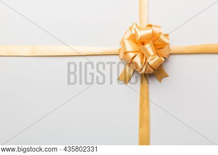 Top View Of Gold Ribbon Rolled And Yellowbow Isolated On Colored Background. Flat Lay With Copy Spac