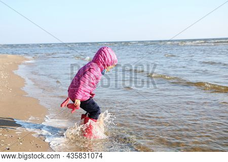 Child Girl Playing By The Sea In Autumn. A Girl In A Red Jacket In A Beautiful Autumn On The Seashor