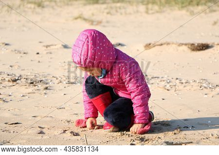 Child Girl Playing By The Sea In Autumn. A Girl In A Red Jacket In A Beautiful Autumn On The Seashor