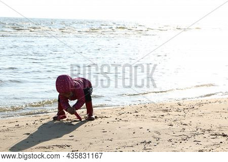 Child Girl Playing By The Sea In Autumn. A Girl In A Red Jacket In A Beautiful Autumn On The Seashor