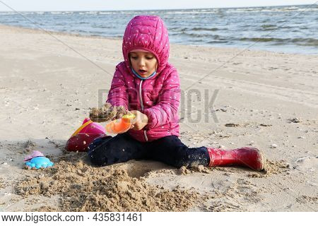 Child Girl Playing By The Sea In Autumn. A Girl In A Red Jacket In A Beautiful Autumn On The Seashor