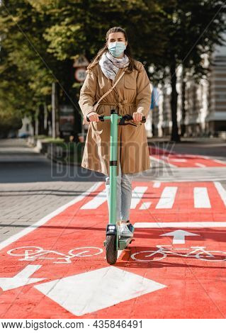 traffic, city transport and people concept - woman in mask riding electric scooter along red bike lane with signs of bicycles and two way arrows on street