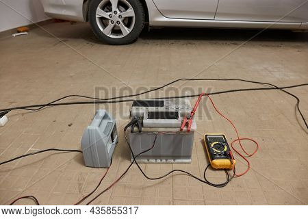 Charging a car starter battery, in a garage, monitoring state with digital multimeter